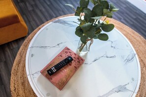 A remote control on a marble table with a vase of green leaves and a book. - Chapel Street Flat 7- Close to Scenic Green Spaces (Long Eaton, Nottingham)
