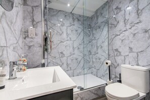Une salle de bain avec un lavabo blanc, des toilettes et une douche à parois de verre.
