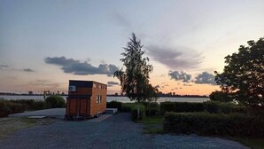 Une petite cabane en bois avec un toit plat, une véranda et une allée de gravier menant à un plan d’eau.