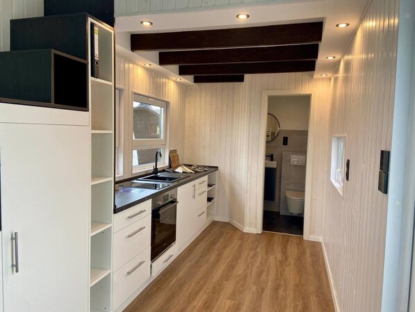 A modern kitchen with white cabinetry, a black countertop, and a built-in oven. - A small house right on the Weser beach (Sandstedt)