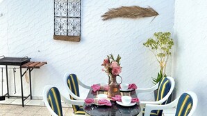 An outdoor patio with a round table, four chairs, a vase with flowers, and a small table with a pitcher.