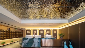 Zona de recepción de un hotel con un mostrador de mármol, dos recepcionistas y estatuas decorativas de perros.
