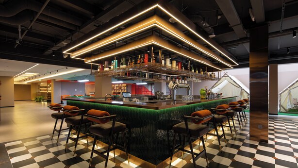 Zona de bar con piso a cuadros, taburetes y barra con detalles en verde.