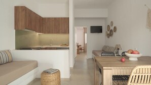 A modern kitchen with wooden cabinets, a dining area with a wooden table and chairs, and a living area with a sofa and a TV mounted on the wall.