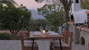 An outdoor dining area with a table set for two, a stone oven, and a view of the sea.