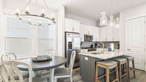 A modern kitchen with white cabinets, stainless steel appliances, and a central island with bar stools.