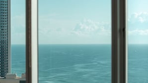 A room with a large window overlooking the ocean, a dining table with chairs, and a view of a tall building across the water. - Skyline on Gold Coast - Stunning Views -38th Floor (Surfers Paradise)
