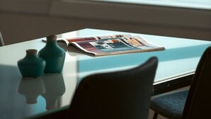 A table with a magazine and two vases, a window with a view of the ocean and a building. - Skyline on Gold Coast - Stunning Views -38th Floor (Surfers Paradise)