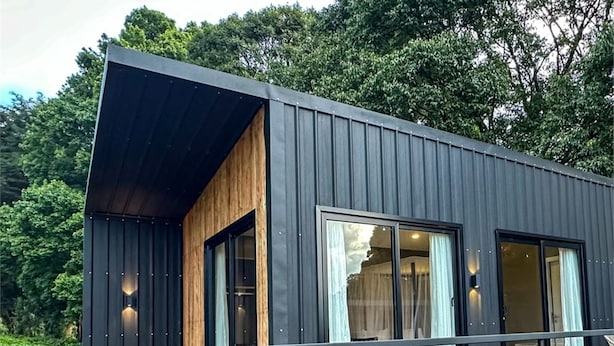 A modern cabin with a wooden deck, large windows, and a dark exterior. - Studio Dwelling (Tigoni)