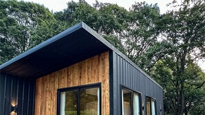 A modern cabin with a wooden exterior, large windows, and a wooden deck. - Studio Dwelling (Tigoni)