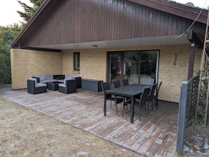 A covered patio with a brick wall, a sliding glass door, and outdoor furniture including a table and chairs. - Lovely summer house in Marielyst (Væggerløse)