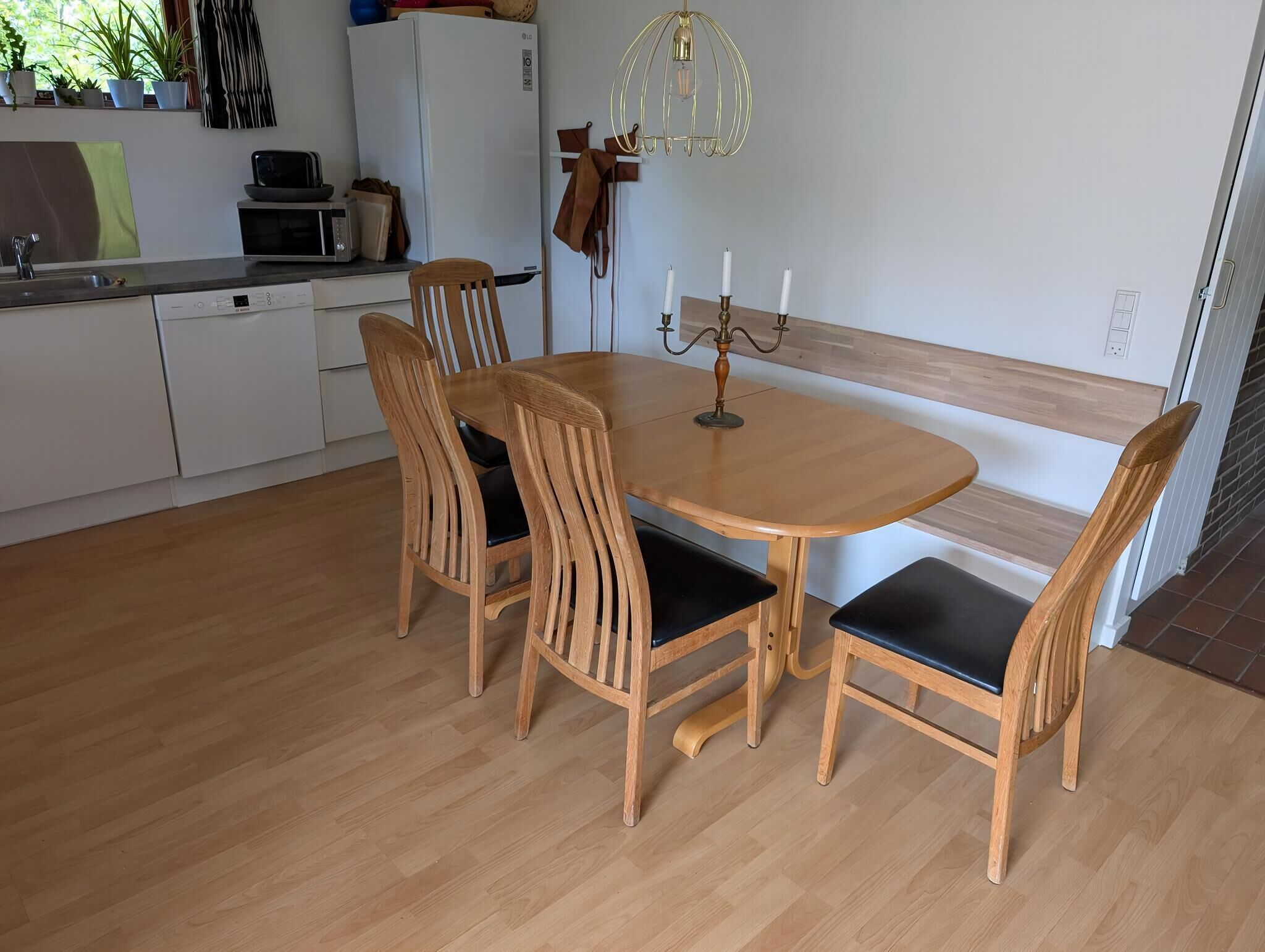 Zona pranzo con tavolo rotondo in legno, quattro sedie, un candelabro e una cucina sullo sfondo.