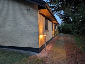 A two-story building with a brick exterior, numbered 12, and a covered porch with outdoor lighting. - Lovely summer house in Marielyst (Væggerløse)