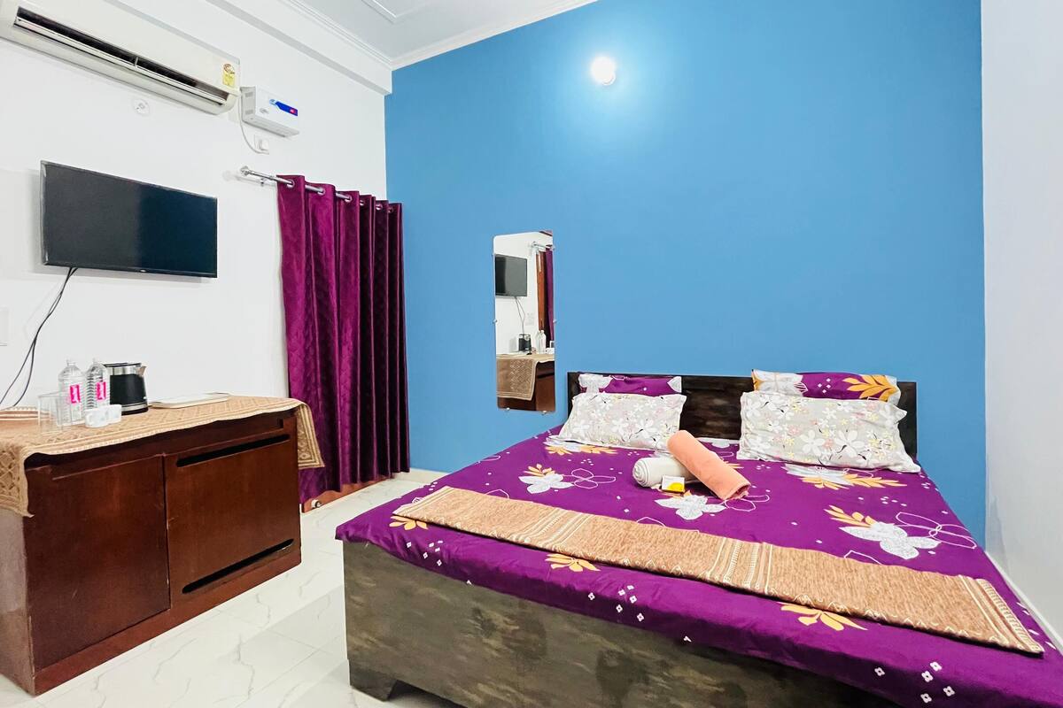 A bedroom with a bed, a TV, a desk, and an air conditioner.