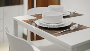 A dining table with white chairs, a white tablecloth, and a placemat. - Gemma by Kozystay - Kebon Jeruk (Jakarta)