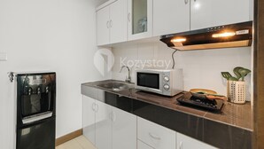 A modern kitchen with white cabinets, a built-in microwave, a water dispenser, and a stove. - Gemma by Kozystay - Kebon Jeruk (Jakarta)