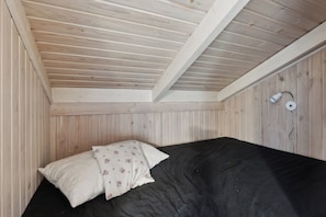 Ein Zimmer mit Holzwänden und -decke, einem Bett mit schwarzer Bettwäsche und einer Wandlampe.