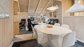 A modern interior with a round dining table, white chairs, a wooden ceiling, and a view of the outdoors. - Cozy summer house near Hals (Hals)