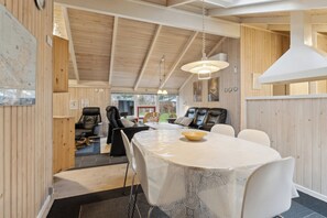 A modern interior with a round dining table, white chairs, a wooden ceiling, and a view of the outdoors.
