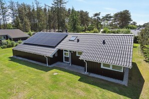 Une maison avec un toit en pente, des panneaux solaires et un petit garage attenant.