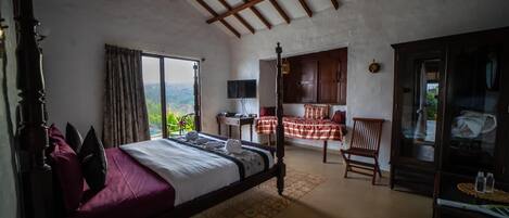 Et soveværelse med himmelseng, stort vindue, udsigt til naturen, garderobeskab i træ og et lille bord med lampe.