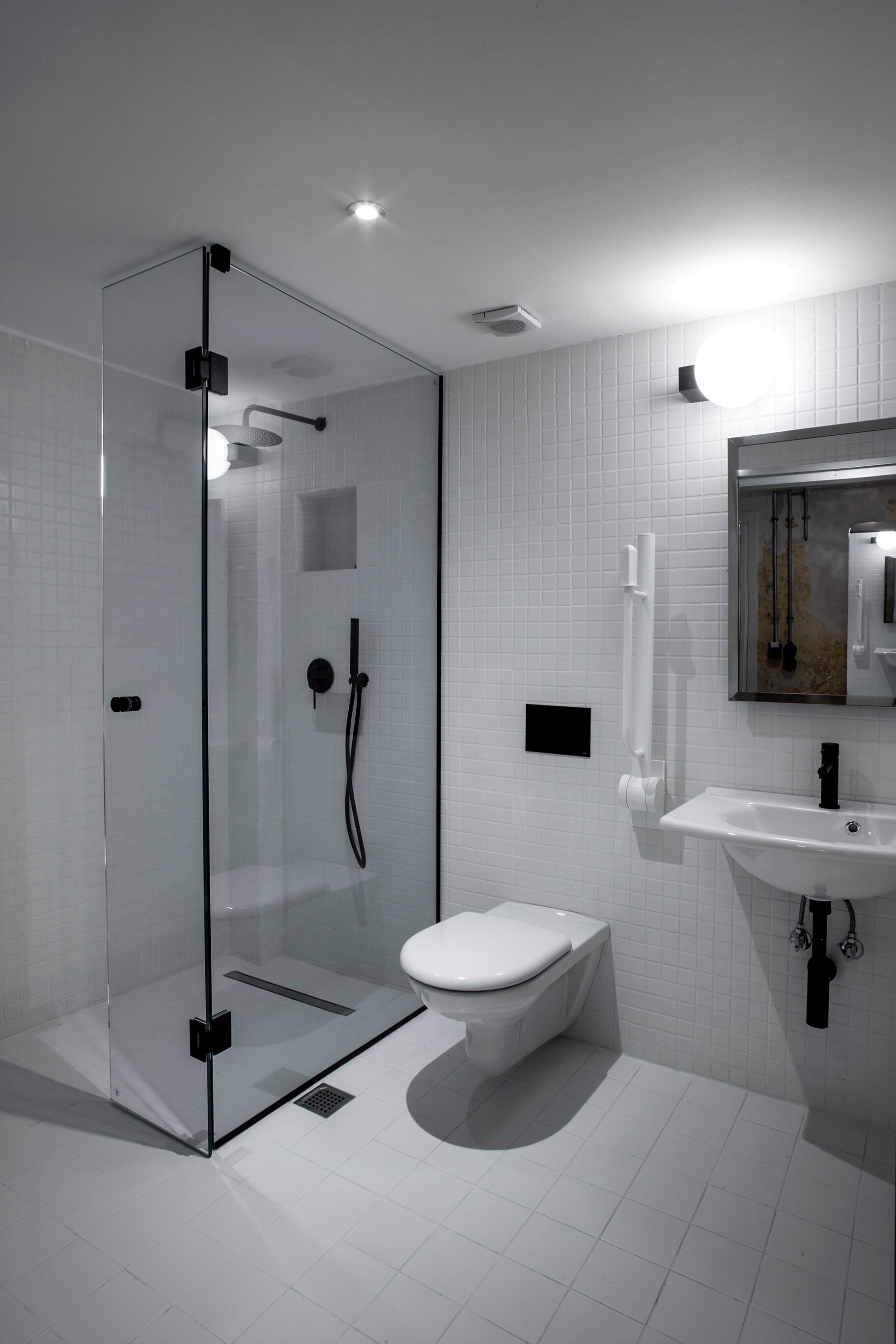 Un baño moderno con ducha envuelta en vidrio, inodoro blanco y lavamanos con espejo superior.