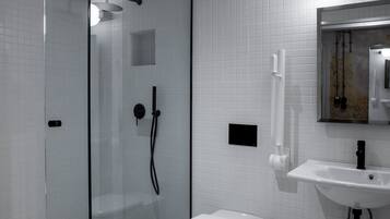 Un baño moderno con ducha envuelta en vidrio, inodoro blanco y lavamanos con espejo superior.