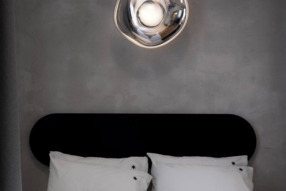 A modern bedroom with a round ceiling light, a black headboard, white bedding, and a grey throw blanket.