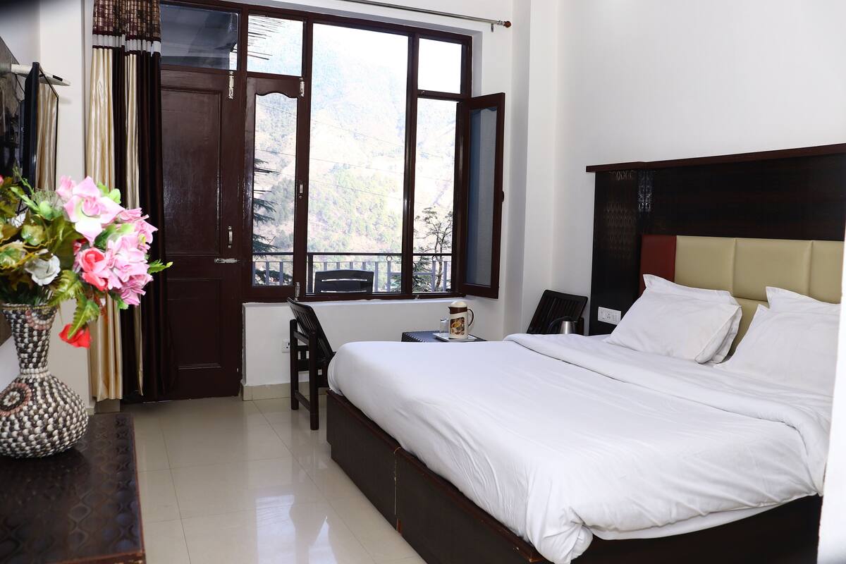 A bedroom with a large bed, a chair, a small table with a cup, and a window with curtains.