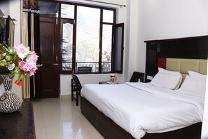 A bedroom with a large bed, a chair, a small table with a cup, and a window with curtains.