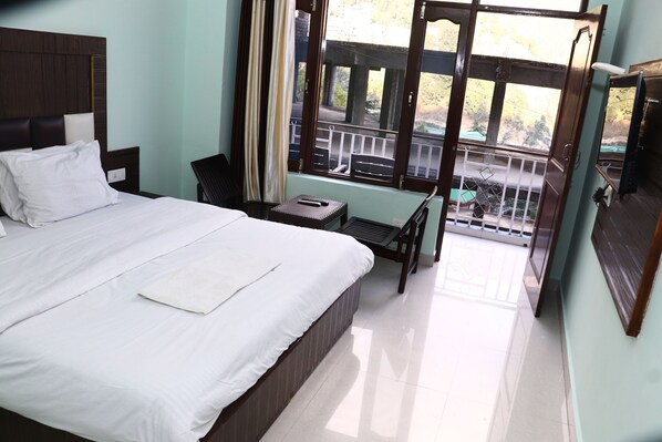 A hotel room with a large bed, a small table, a chair, and a balcony with a railing.