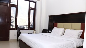 A neatly made bed with white linens, a wooden headboard, and a window with a view of a mountain. - Hotel Hillora Mcleodganj (Dharamshala)
