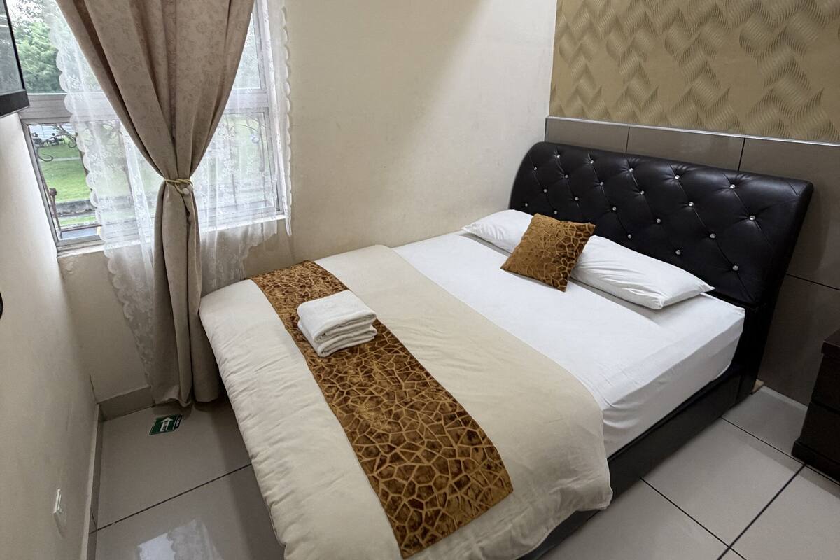 Una habitación de hotel con cama, cortinas, cabecero y pared con estampado.
