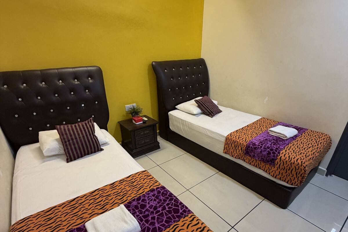 Habitación de hotel con dos camas, una mesita de noche y una pared amarilla.