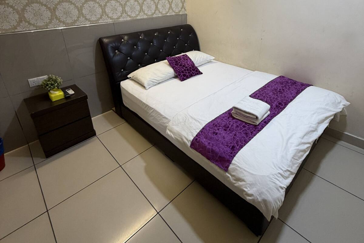 Un dormitorio ordenado con una cama, una mesita de noche y una pared con papel tapiz estampado.
