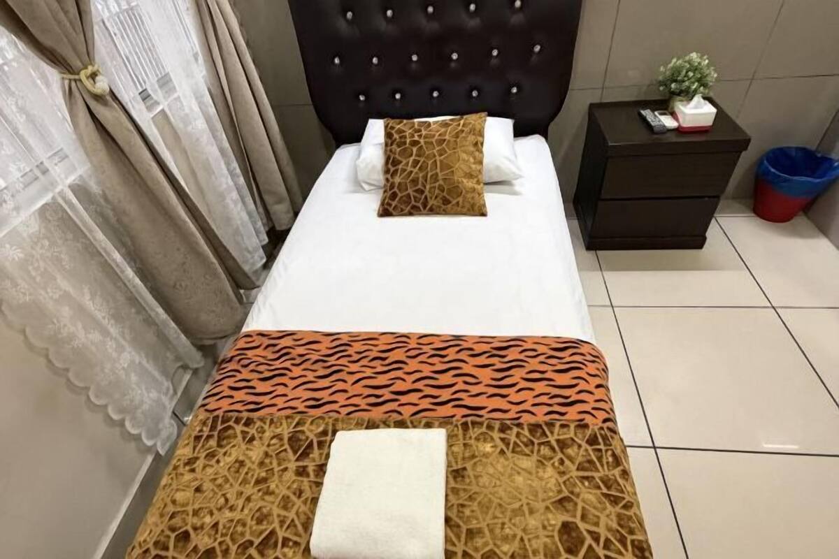 Una habitación de hotel con una cama, una mesita de noche, una planta pequeña y un cubo de basura.
