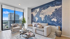 Una sala de estar moderna con un mural grande de un mapa mundial, un sofá, dos sillones, una mesita de centro y vistas de la ciudad a través de amplios ventanales.