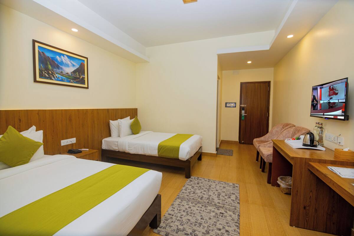 A hotel room with two beds, a desk, a TV, and a painting on the wall.