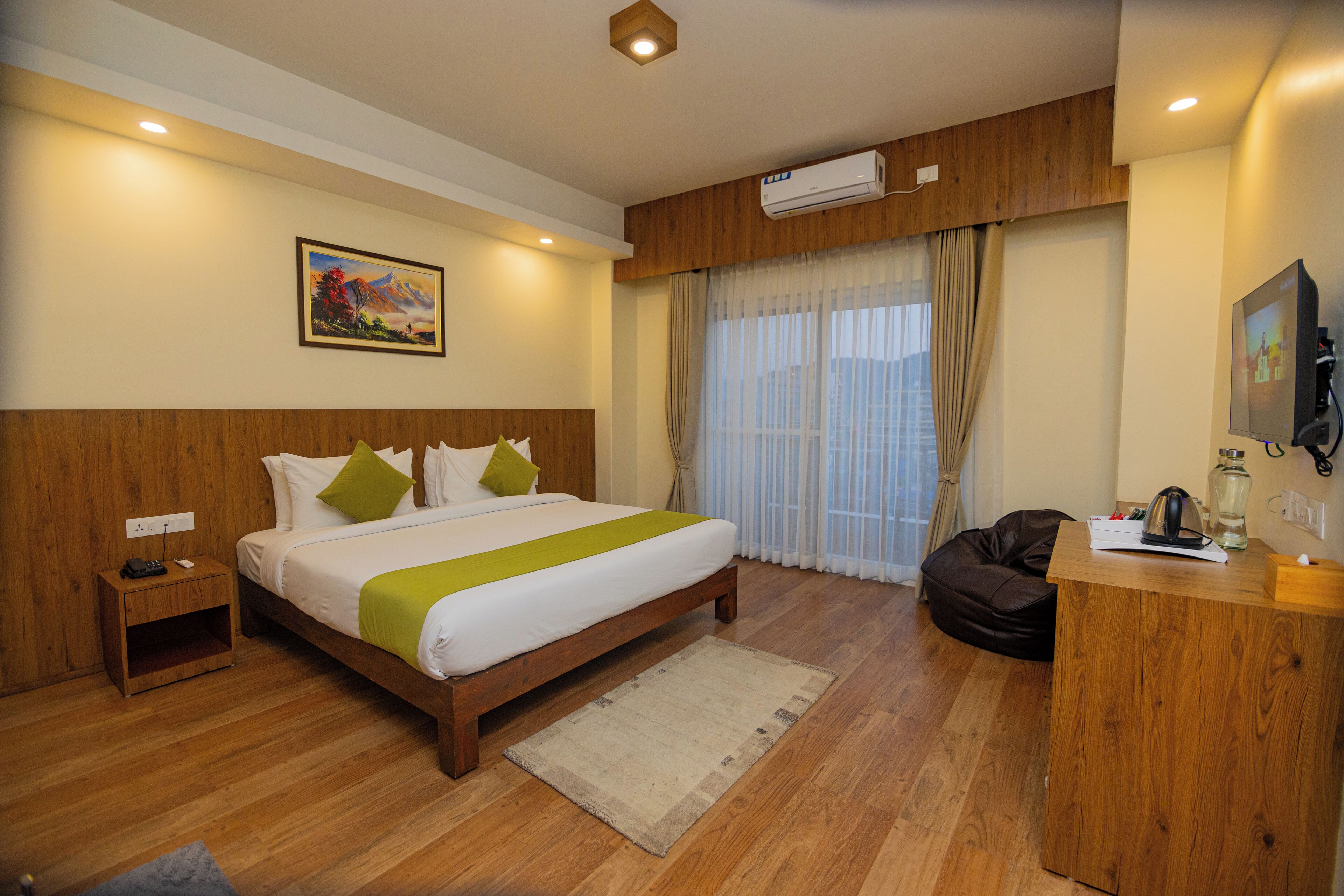 A hotel room with a wooden bed, a desk, a chair, a nightstand, a window with curtains, and an air conditioning unit.