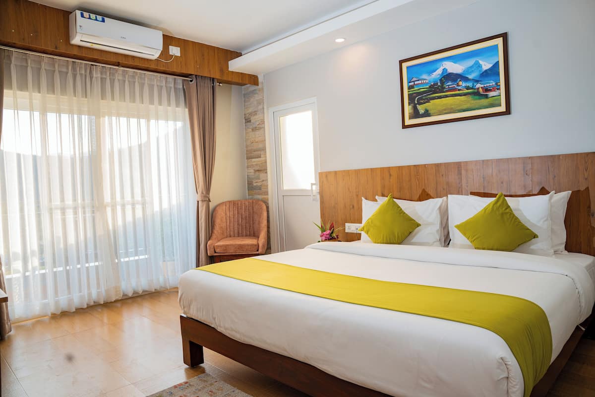 A hotel room with a large bed, wooden headboard, a painting on the wall, and a window with curtains.