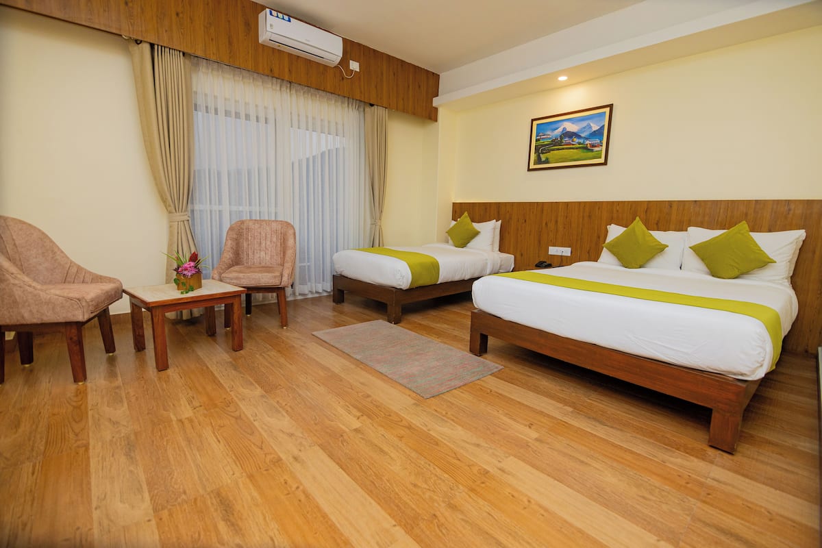 A hotel room with two beds, a wooden floor, a desk, a chair, and a painting on the wall.