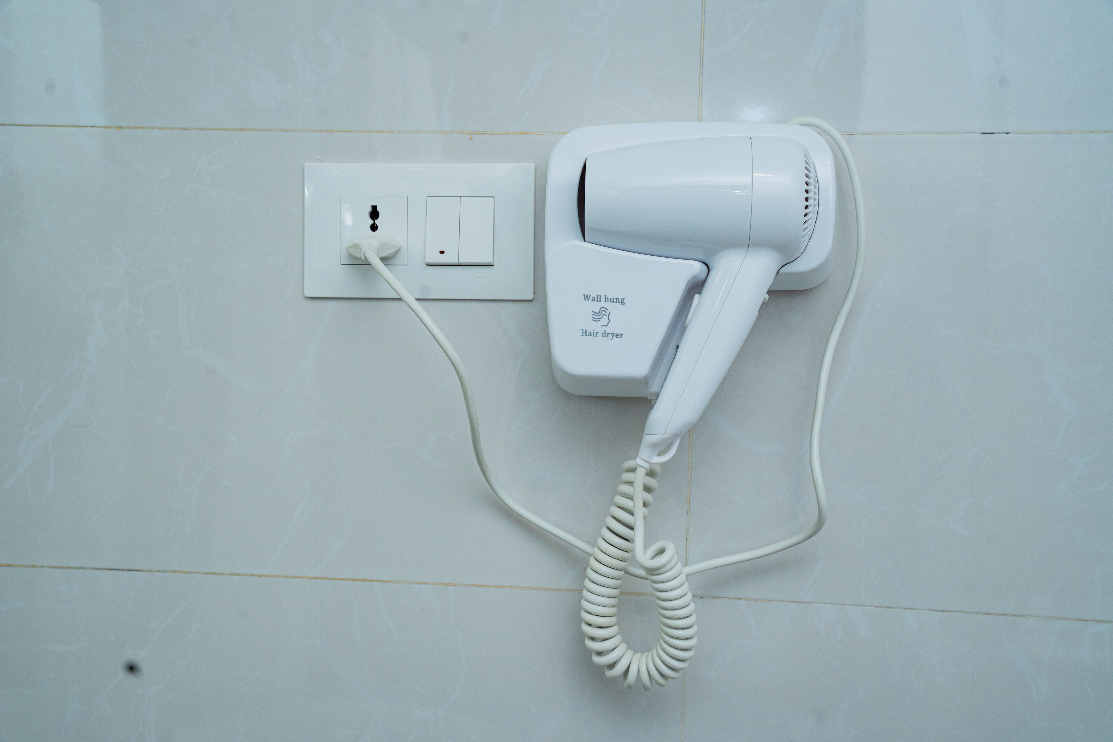 A hair dryer mounted on a wall next to a power outlet.