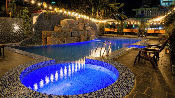 A nighttime swimming pool with a blue mosaic edge, stone steps, and string lights.