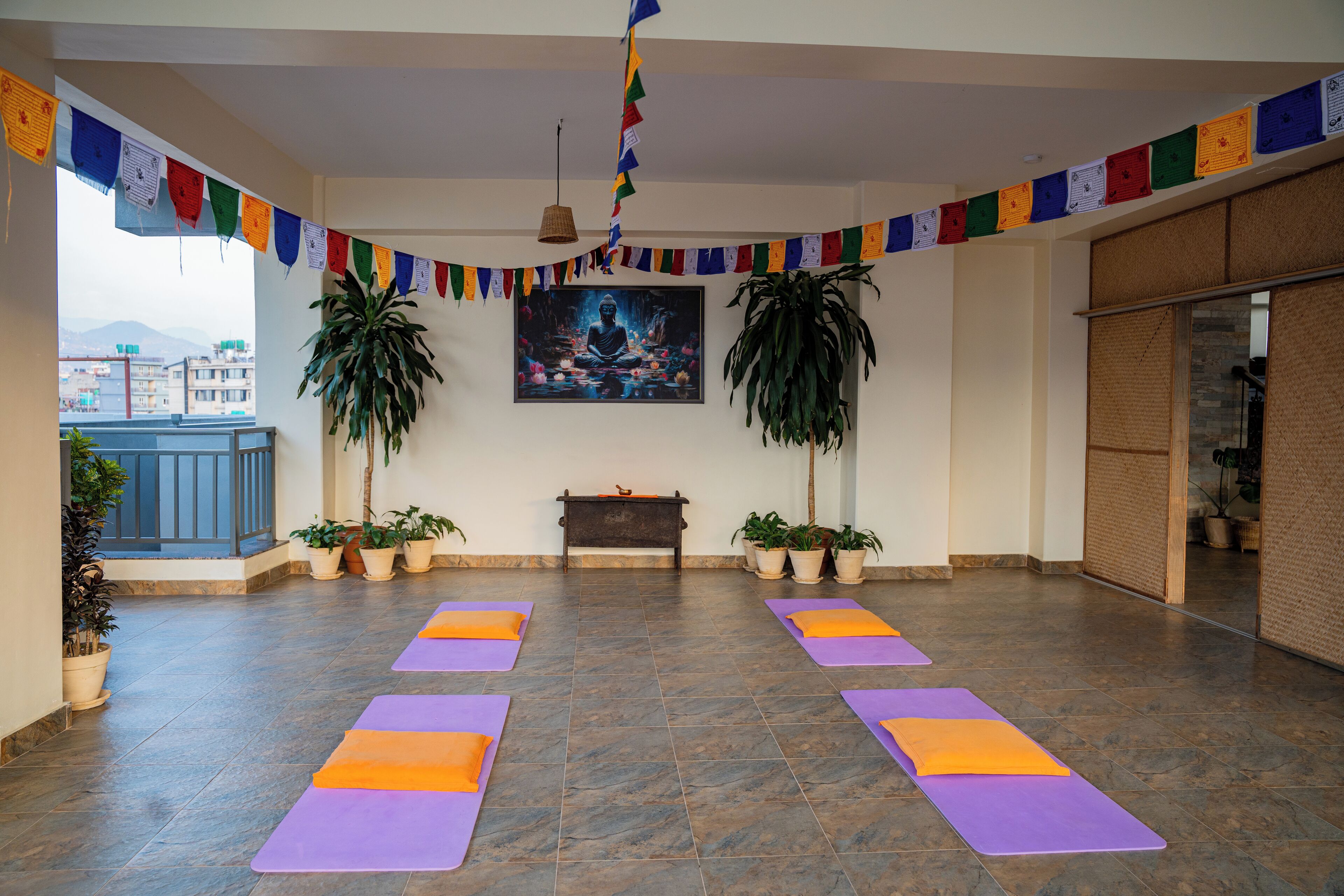 A yoga studio with mats, a painting, prayer flags, and potted plants.