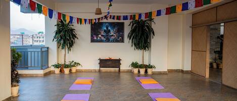 A yoga studio with mats, a painting, prayer flags, and potted plants.