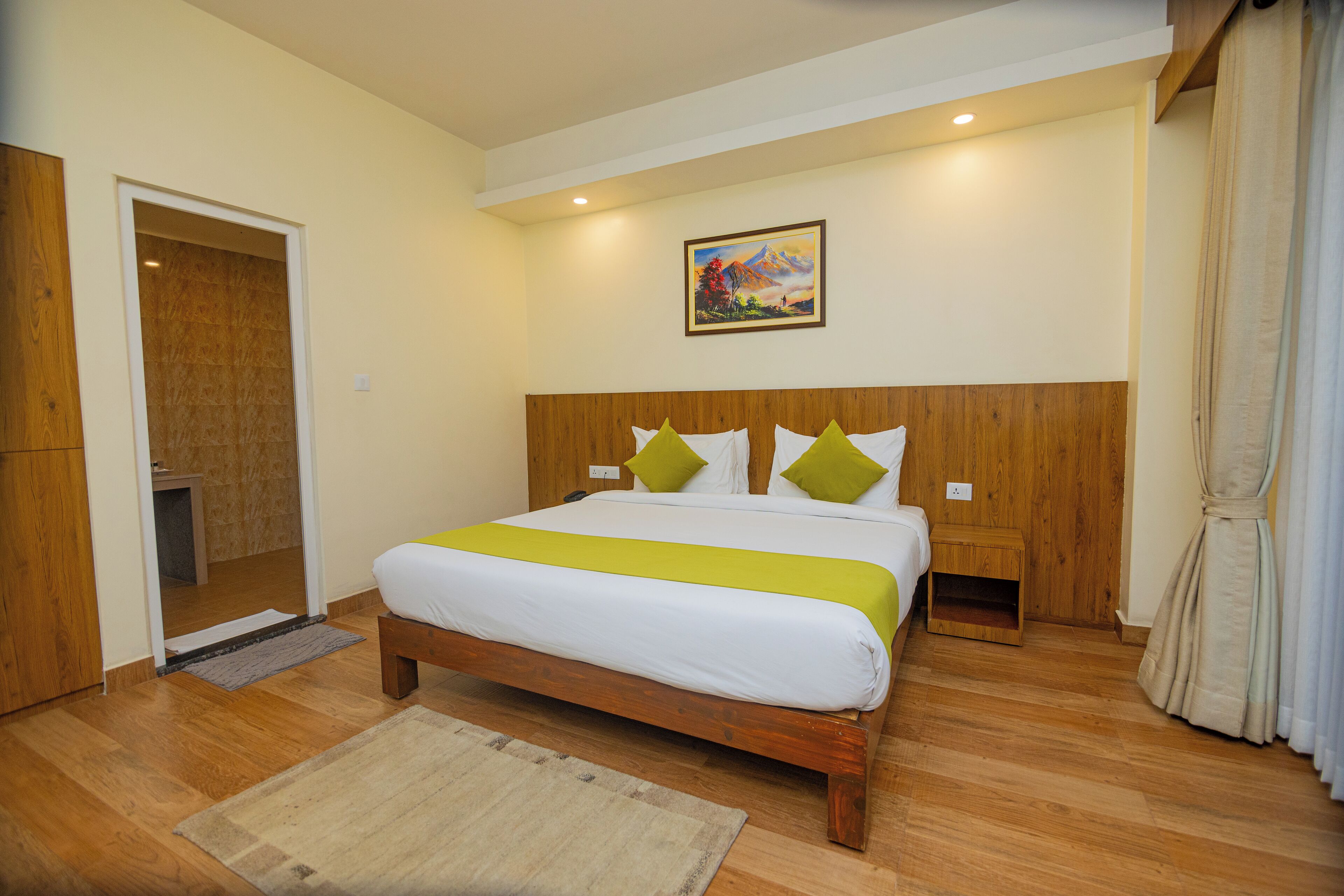 A bedroom with a wooden bed, white bedding, green pillows, a painting on the wall, and a wooden wardrobe.