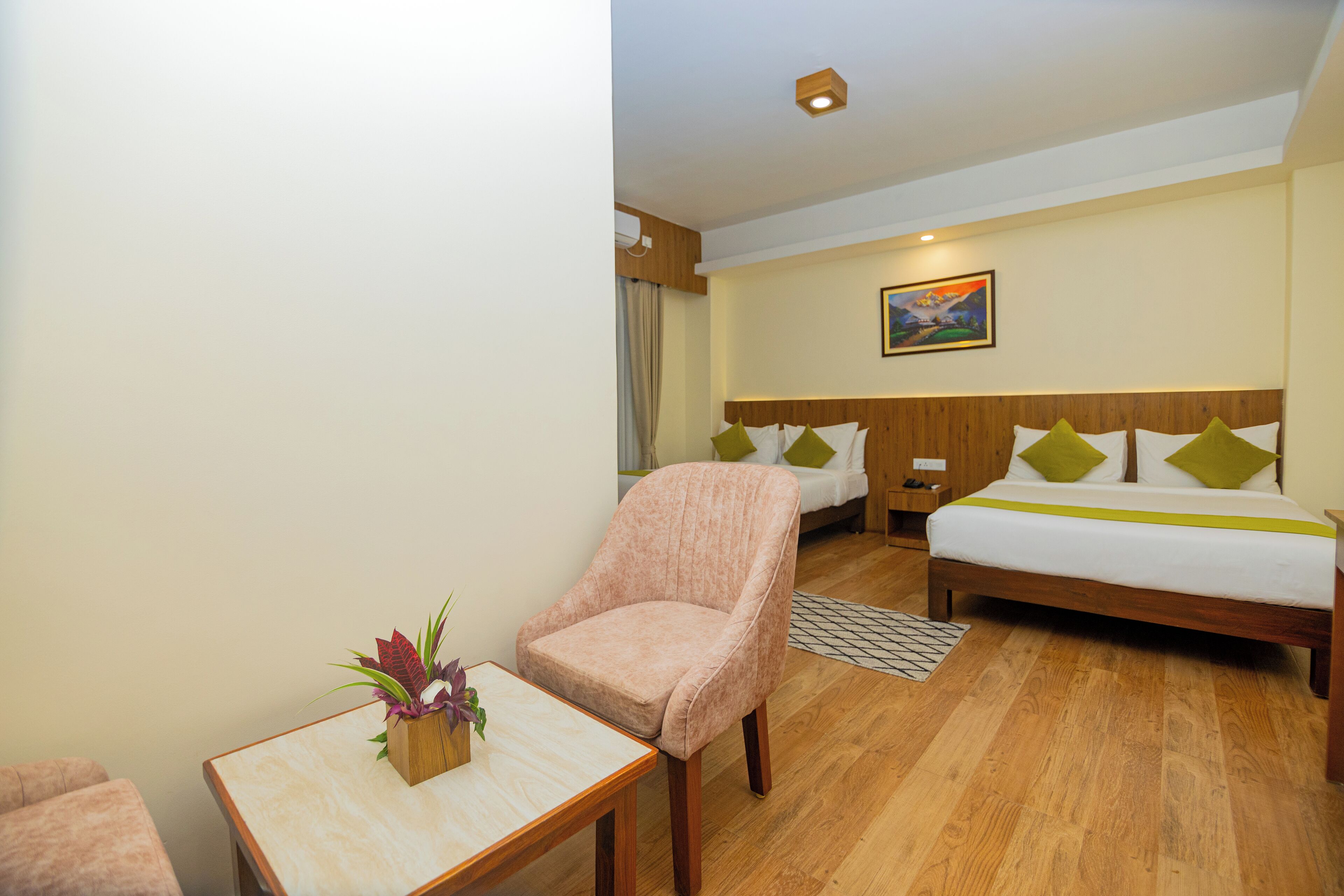 A hotel room with a bed, a chair, a small table with a plant, and a painting on the wall.