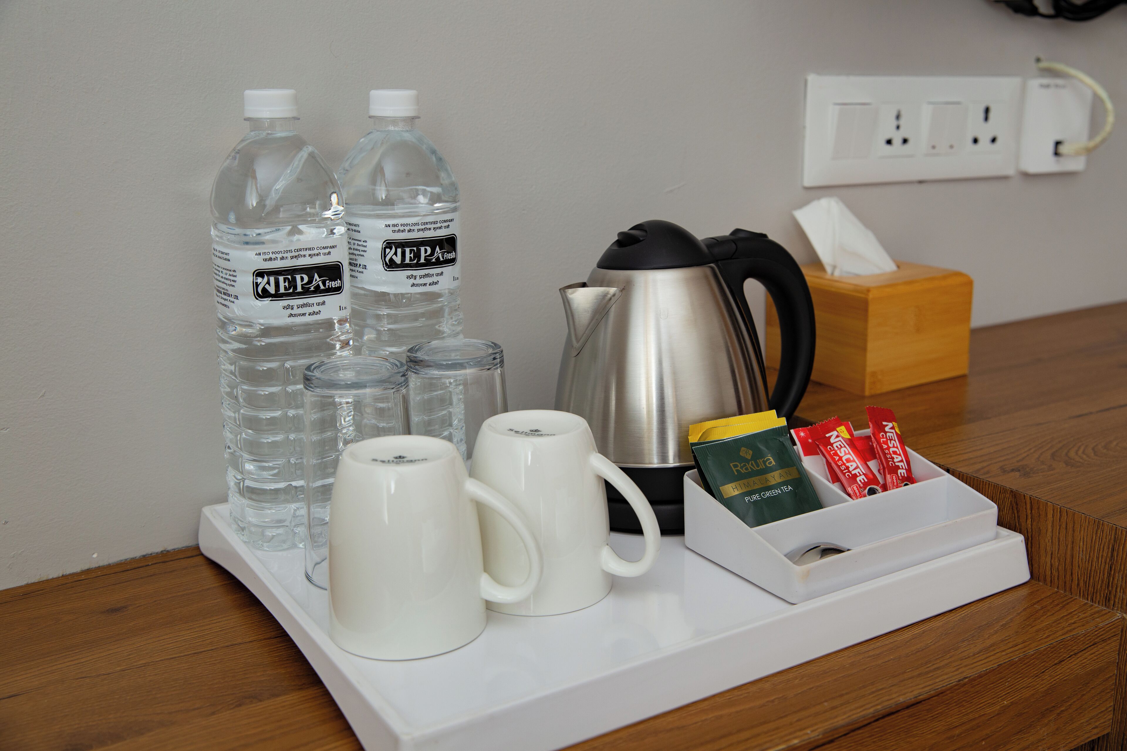 A table with water bottles, coffee maker, mugs, and a tissue box.