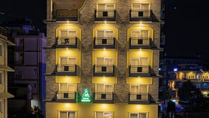 A multi-story hotel with balconies, a swimming pool, and a well-lit entrance.