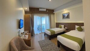 A hotel room with two beds, a desk with a chair, a television, and a window with curtains.